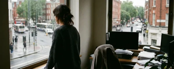 Un salarié vu de dos regarde par la fenêtre d'un bureau avec lumière naturelle de fin de journée.